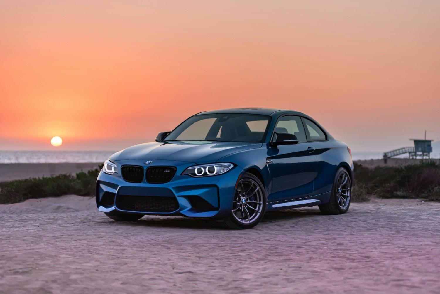 A modern sleek blue car driving on a scenic coastal highway during sunset